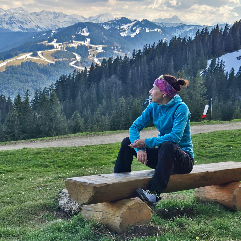 reflexionsfragen-jahresrückblick Frau sitzt auf Bank mit Bergpanorama im Hintergrund und schaut in die Ferne